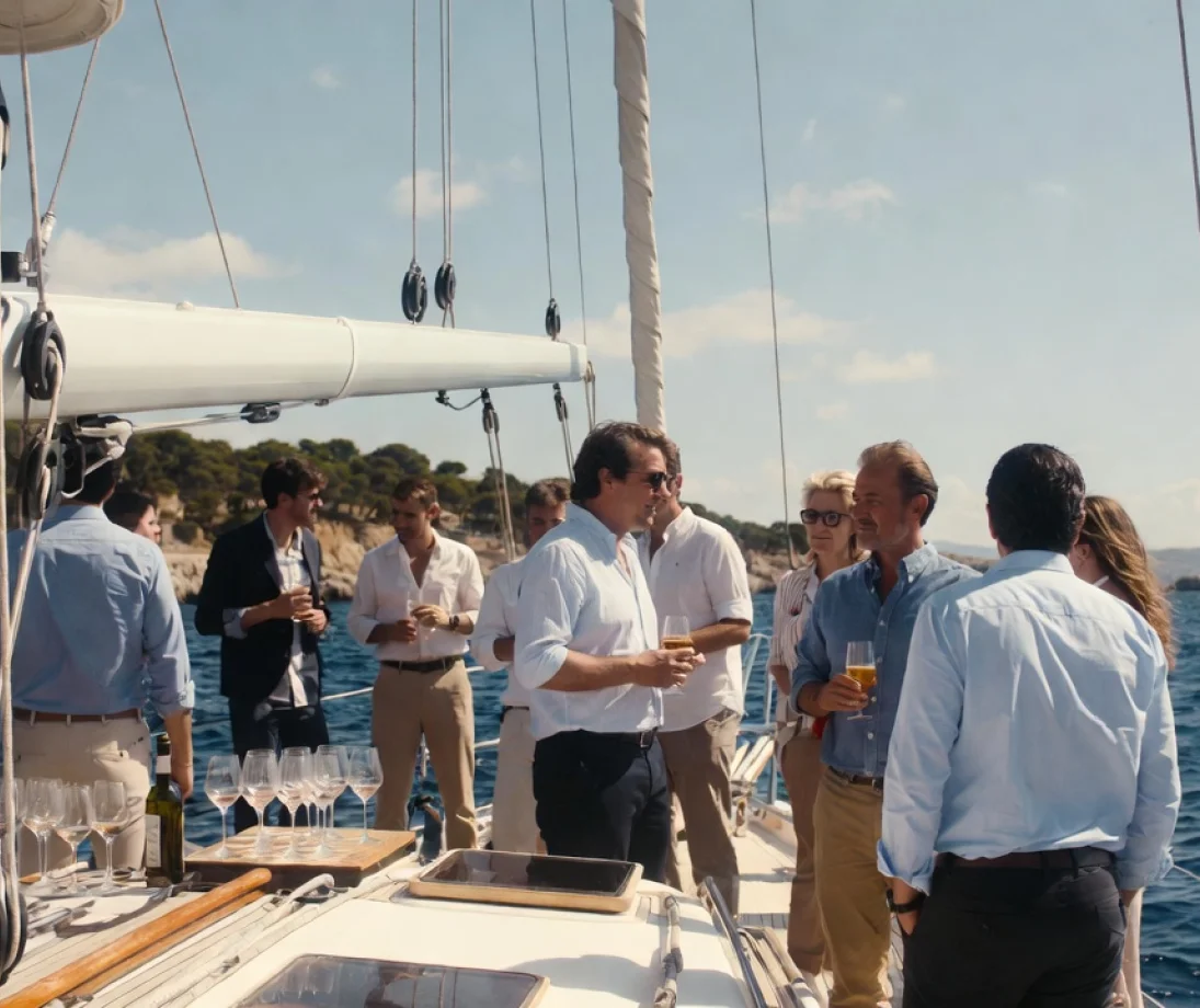 Tre persone che parlano rilassate su uno yacht di lusso di fronte allo skyline di Barcellona al tramonto