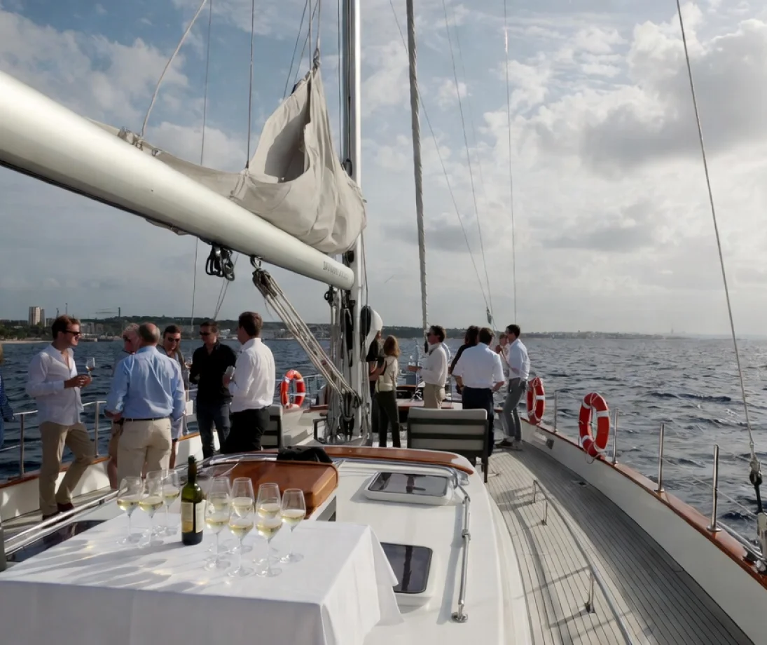 Three people talking casually on a luxury sailboat in front of the Barcelona skyline at sunset