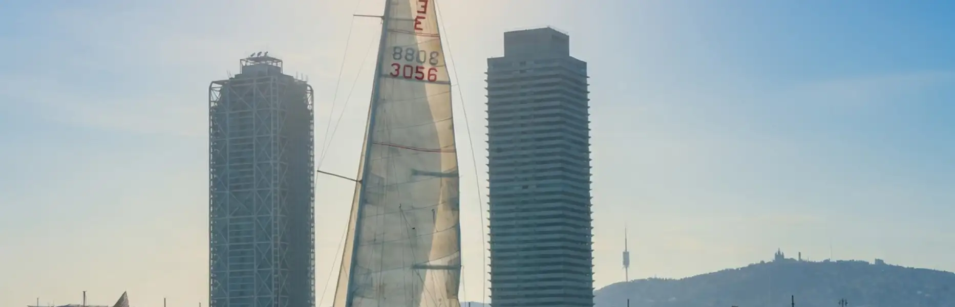 Veliero che naviga davanti allo skyline di Barcellona con il sole basso e il mare calmo