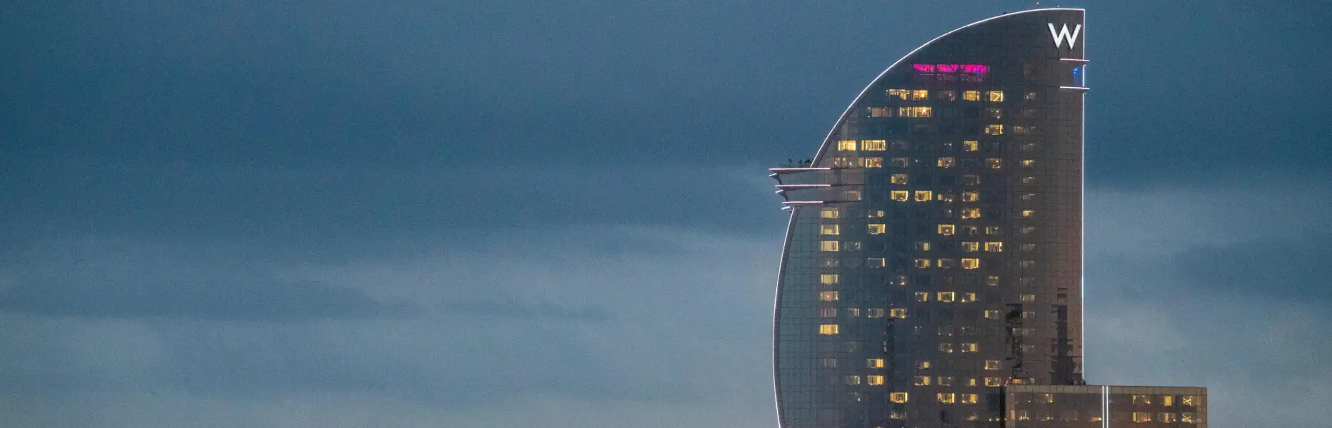 Vue de l’hôtel W de Barcelone au coucher du soleil, en bord de mer, avec les lumières allumées et un ciel nuageux