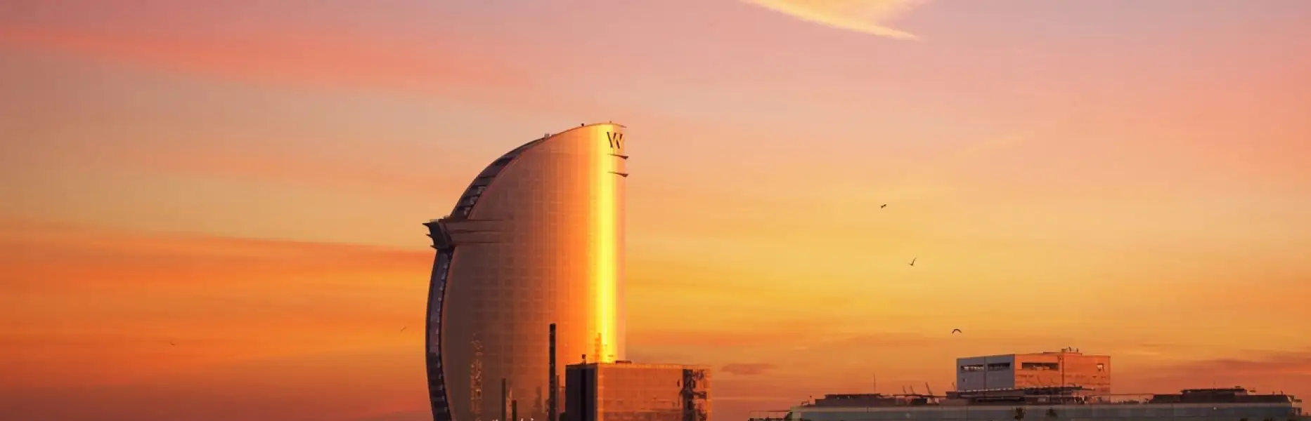 Lever de soleil doré sur l'hôtel voile de Barcelone vu depuis la mer à bord d'un voilier privé