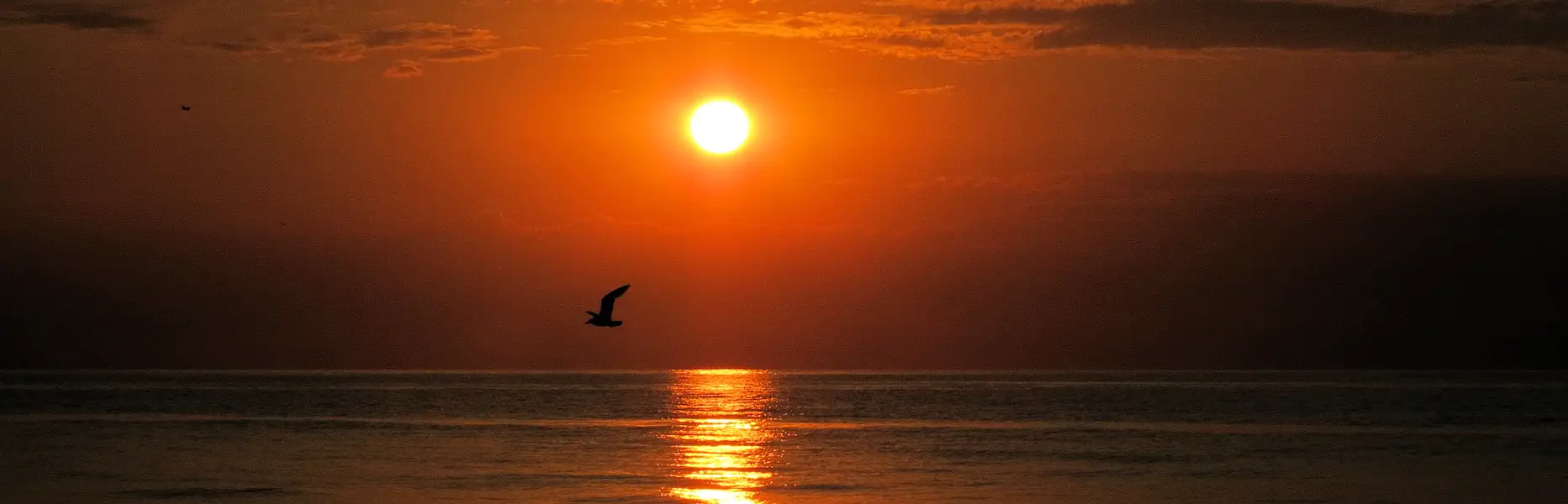 Die Sonne geht über dem ruhigen Meer auf, mit einer Segelyacht im Morgengrauen vor Barcelona