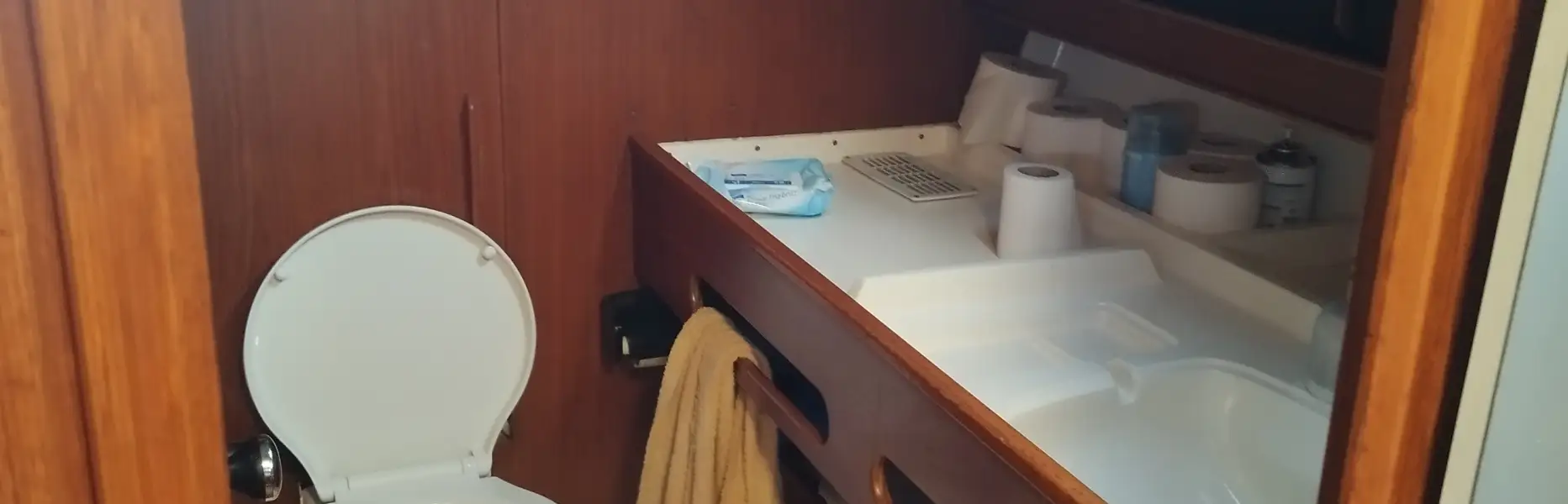 Private bathroom on a sailboat with marine toilet, sink and towels in a wooden cabin