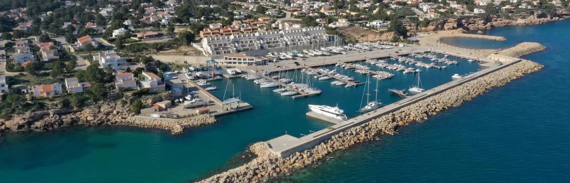 Aerial view of a marina with sailing boats moored along the coast, mountains in the background, near the Ebro Delta