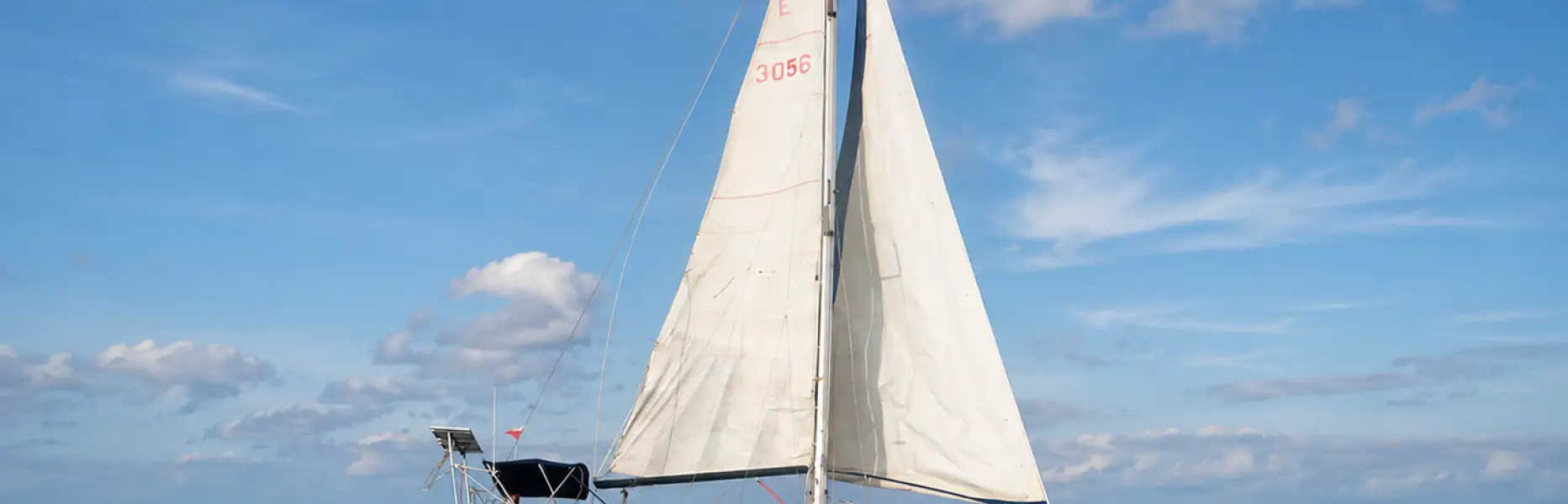 Velero de crucero navegando a vela en mar abierto bajo un cielo azul con nubes dispersas