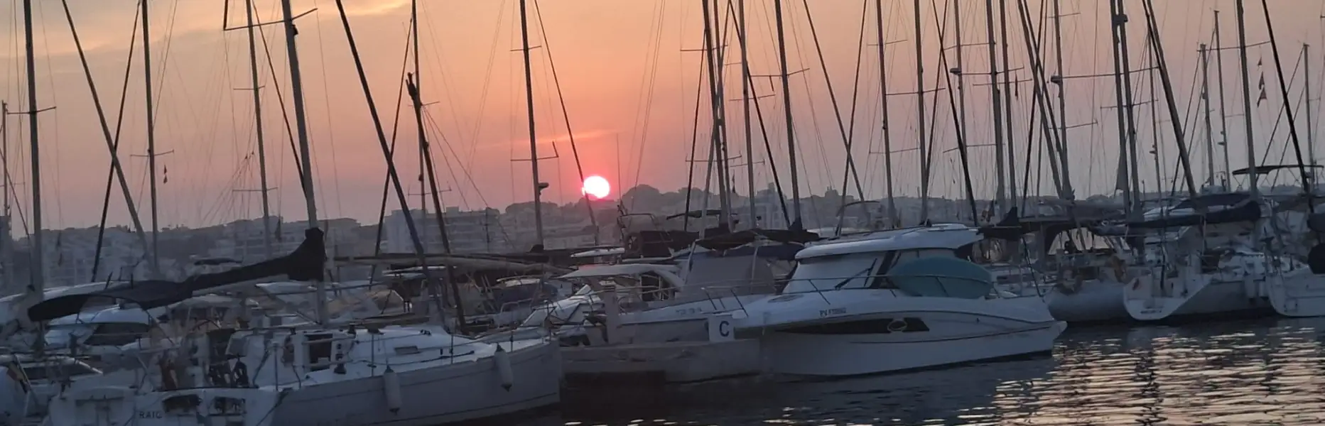 Tramonto rosato su un porto con barche a vela ormeggiate e il sole che si riflette nel mare a Barcellona