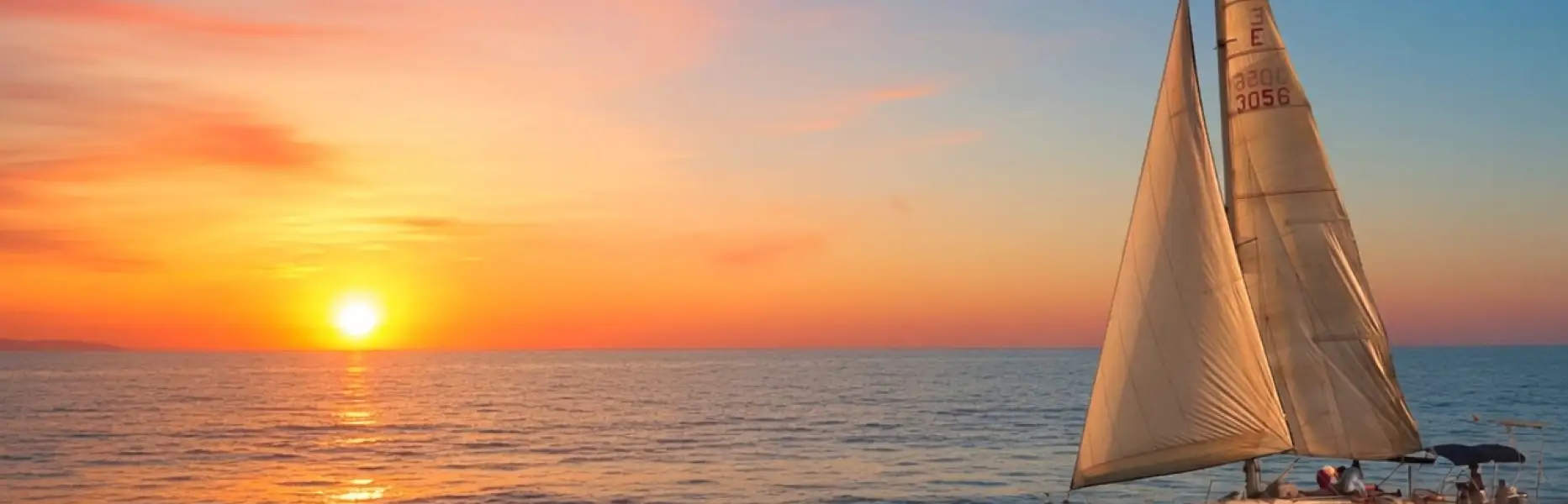 Segelboot bei Sonnenaufgang mit der Sonne, die über dem Meer vor Barcelona aufgeht