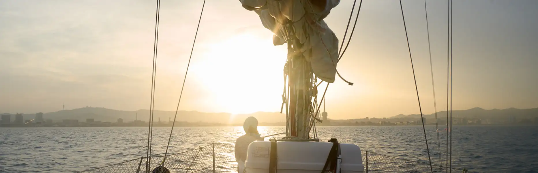 Vista desde la cubierta de un velero al atardecer en Barcelona con el sol sobre el mar