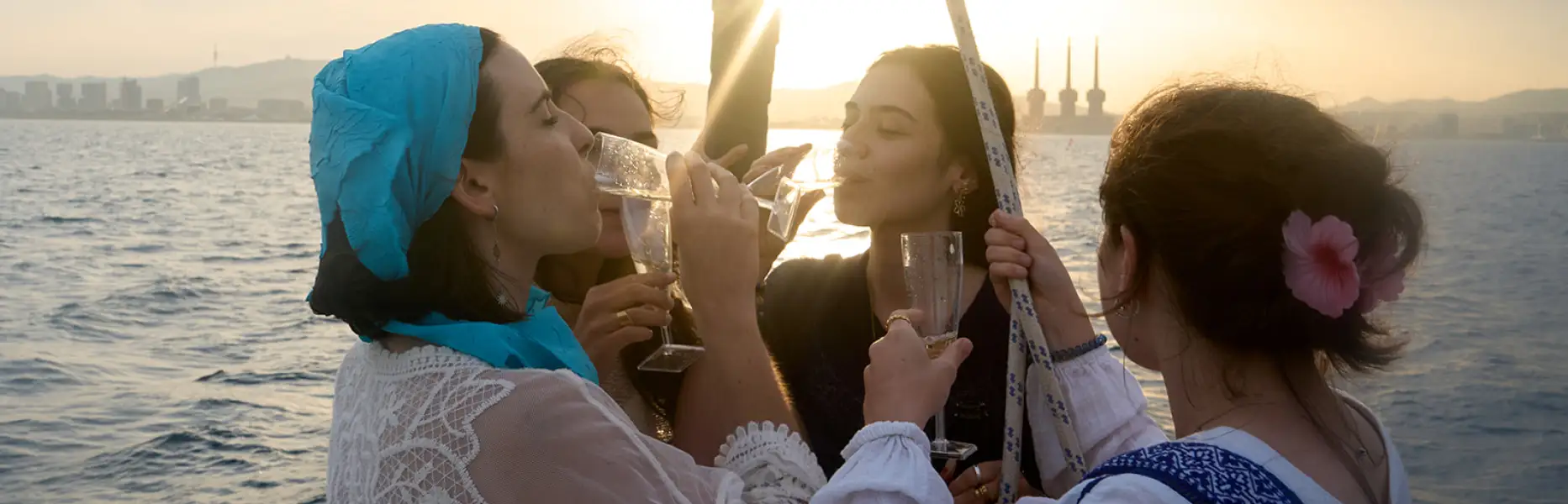 Grupo de amigas brindando con cava al atardecer en un barco frente a la costa de Barcelona