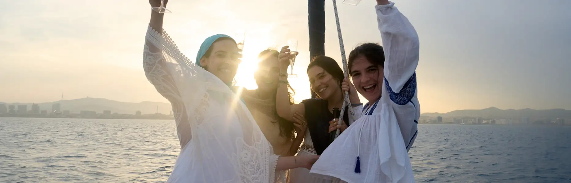 Grupo de amigas brindando con cava al atardecer en un barco frente al skyline de Barcelona