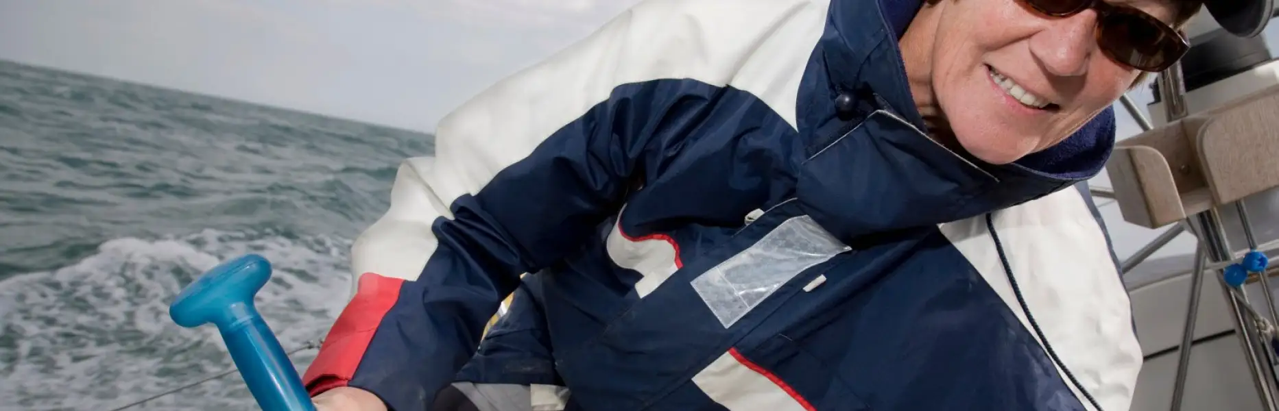 Donna sorridente che naviga una barca a vela in mare aperto durante un charter
