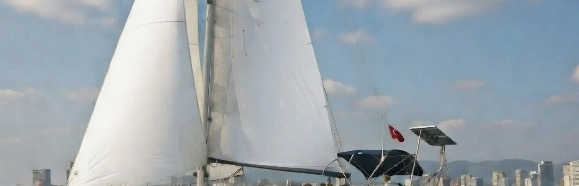 Barca a vela che naviga davanti allo skyline di Barcellona in una giornata soleggiata con mare calmo
