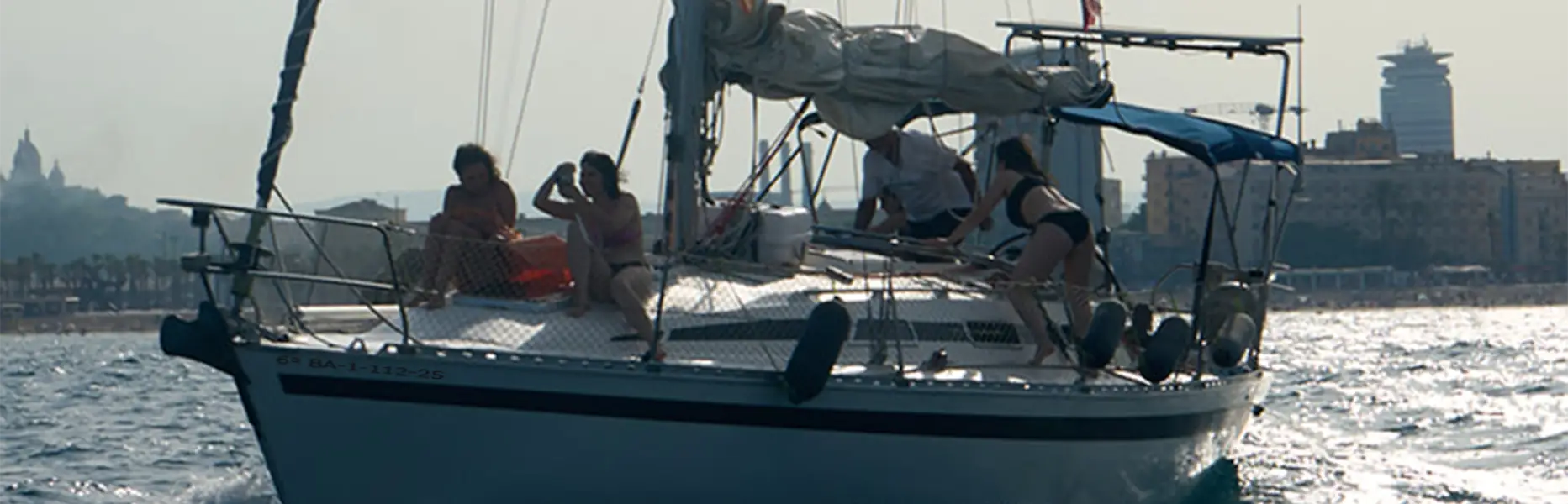 Gruppe von Menschen, die bei Sonnenuntergang vor der Küste Barcelonas einen Segelausflug genießen