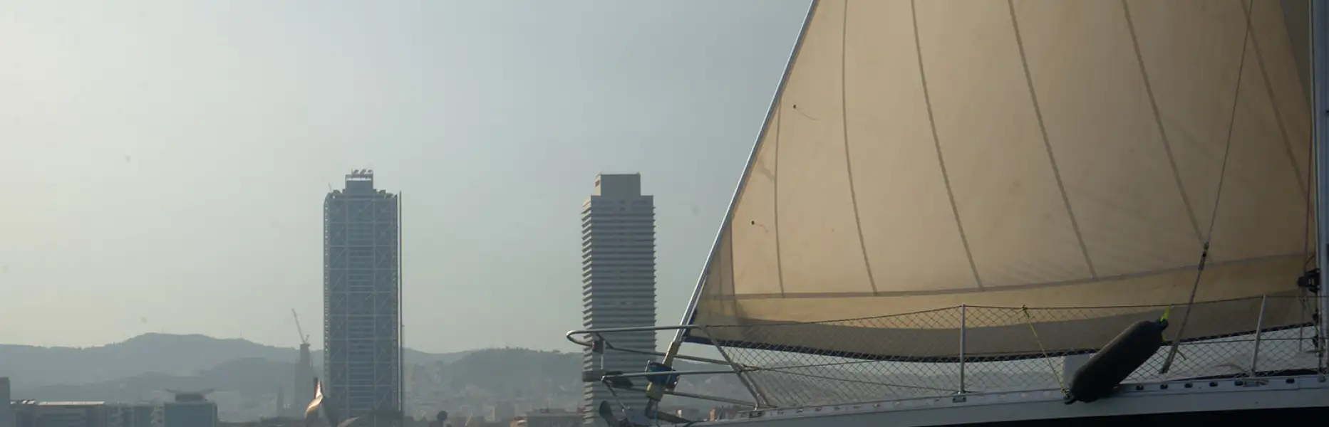 Velero de charter navegando cerca de la costa de Barcelona con rascacielos al fondo en un día despejado
