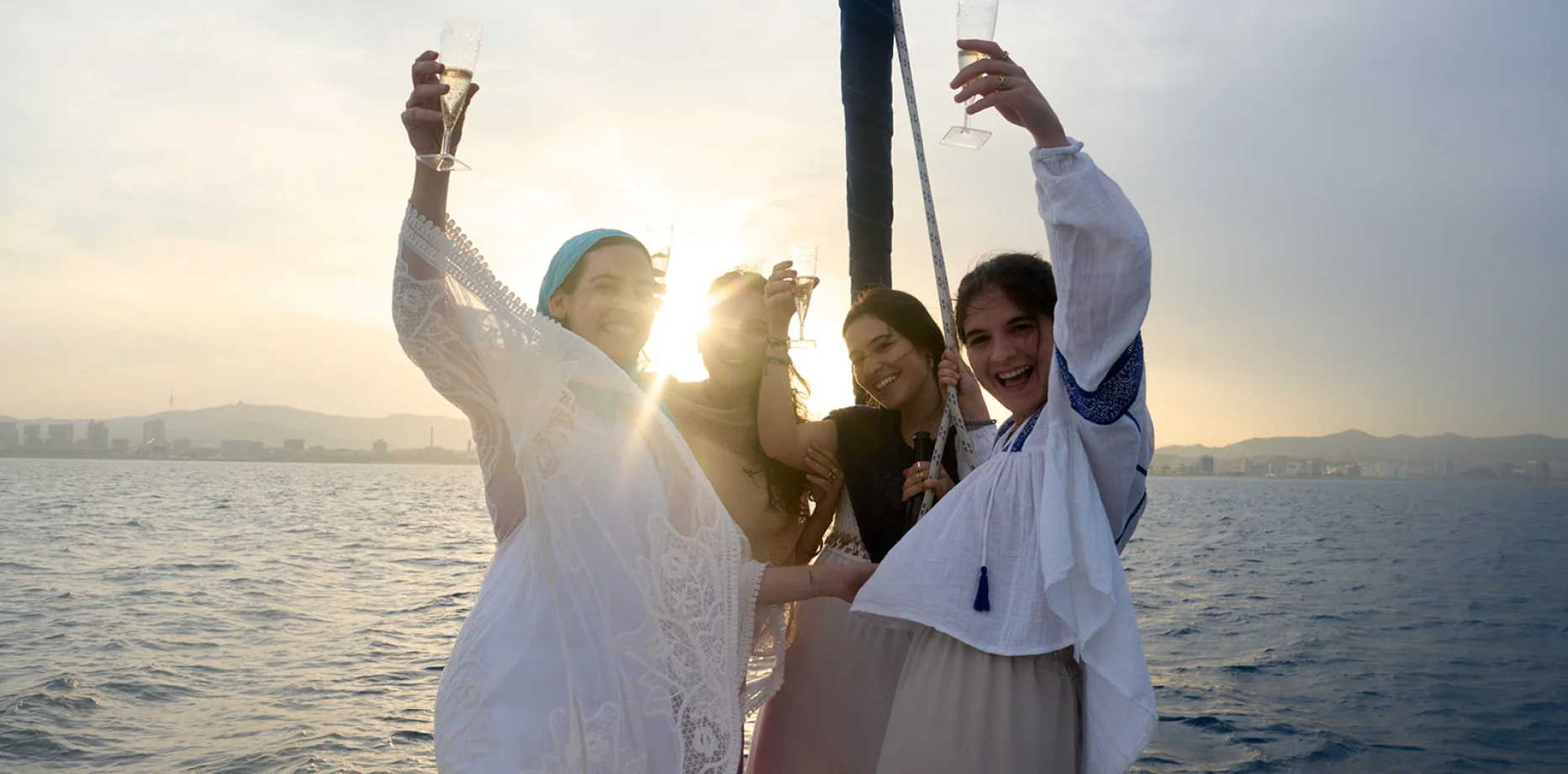Group of professionals enjoying wine and appetisers on a sailboat in front of the Barcelona skyline at sunset