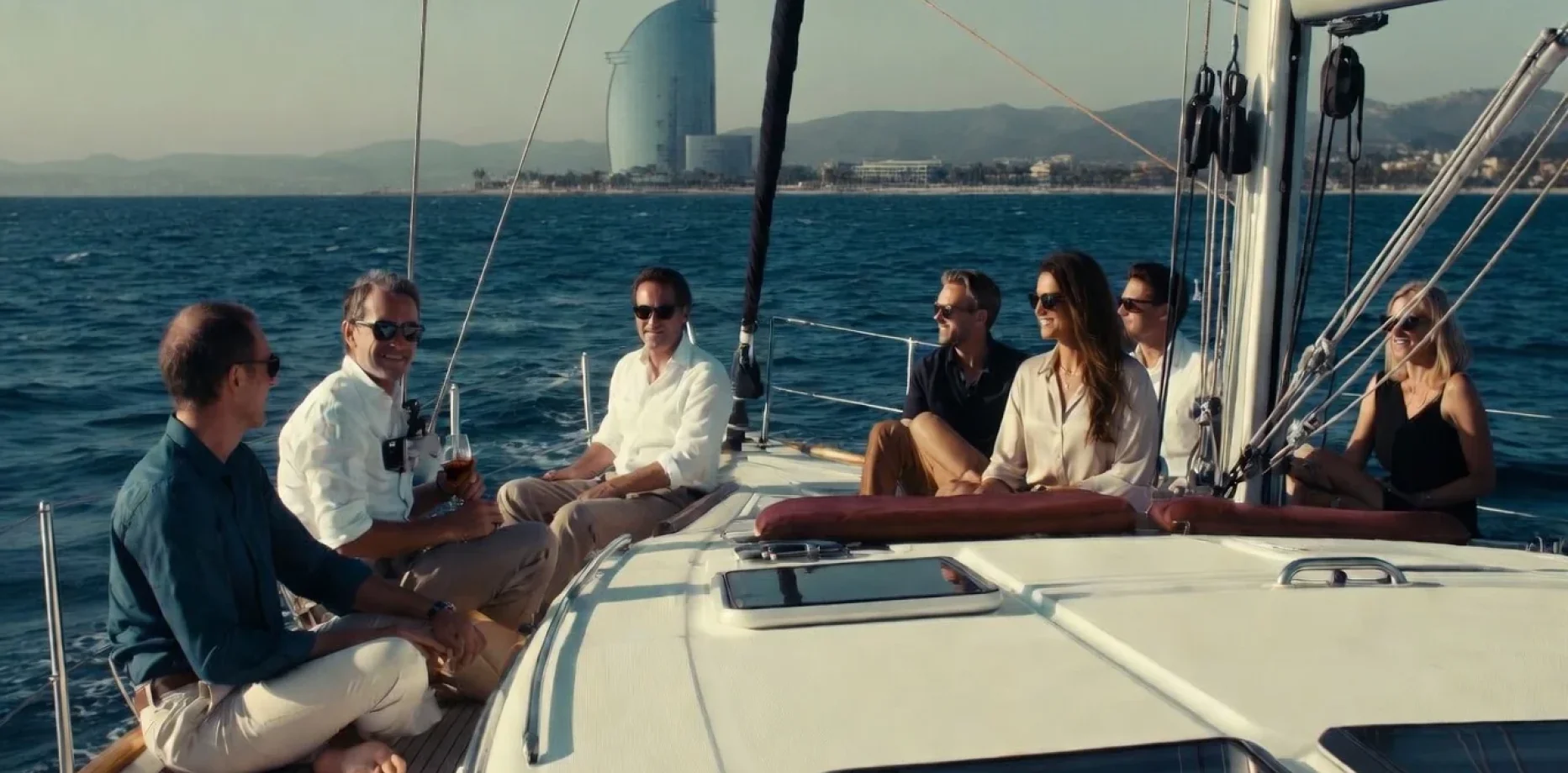 Gruppo di professionisti che gustano vino e aperitivi su una barca a vela davanti allo skyline di Barcellona al tramonto