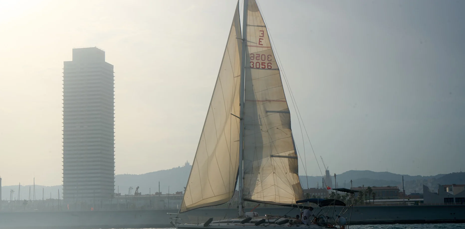 Grupo de profesionales disfrutando de vino y aperitivos en un velero frente al skyline de Barcelona al atardecer
