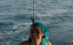 Mujer joven sonriendo mientras navega un velero privado frente a la costa de Barcelona