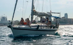 Velero con grupo de amigos disfrutando de un charter privado frente al skyline de Barcelona