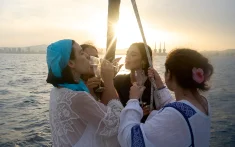 Grupo de amigas brindando con cava al atardecer en un barco frente a la costa de Barcelona