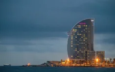 Blick auf das W Hotel in Barcelona bei Sonnenuntergang am Meer mit eingeschalteten Lichtern und bewölktem Himmel