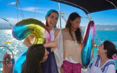 Kleine Freundinnengruppe, die eine Bootstour vor der Skyline von Barcelona mit bunten Luftballons genießt