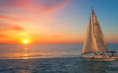 Velero navegando al amanecer con el sol saliendo sobre el mar en Barcelona