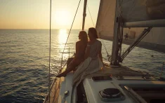 Two people enjoy the sunrise over the Mediterranean Sea from the bow of a sailboat in Barcelona