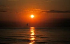 Sun rising over a calm sea with a sailboat at dawn off the coast of Barcelona