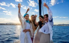Group of friends toasting with cava on the bow of a private sailboat off the coast of Barcelona at sunset