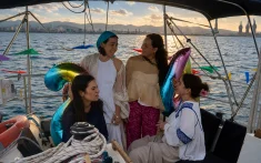 Gruppe von Freundinnen, die einen Geburtstag auf einer privaten Segelyacht vor der Küste von Barcelona bei Sonnenuntergang mit Luftballons und Dekoration feiern
