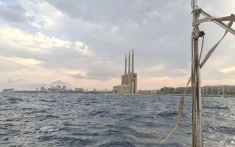 Vista des d’un veler navegant davant la costa de Barcelona amb mar lleugerament mogut i les tres xemeneies al fons