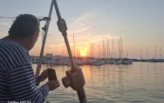 Patró en un veler privat observant la posta de sol sobre el port esportiu de Barcelona amb nombrosos velers amarrats