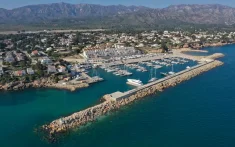 Vista aérea de un puerto deportivo con veleros amarrados junto a la costa y montañas al fondo cerca del Delta del Ebro