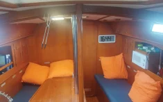 Interior de velero con salón de madera, cojines naranjas y reloj digital preparado para la expedición al eclipse total de Sol