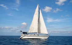 Velero de crucero navegando a vela en mar abierto bajo un cielo azul con nubes dispersas