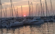 Atardecer rosado sobre un puerto con veleros amarrados y el sol reflejándose en el mar en Barcelona