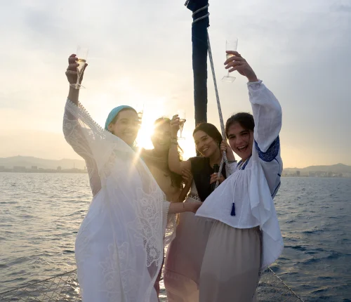 Grupo de amigas brindando con cava al atardecer en un barco frente al skyline de Barcelona