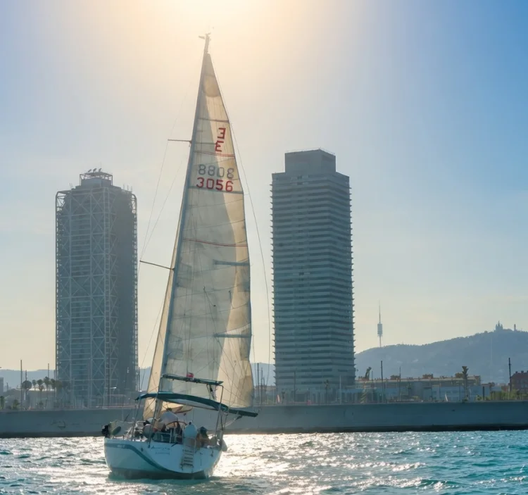 Sailboat sailing in front of the Barcelona skyline with low sun and calm sea