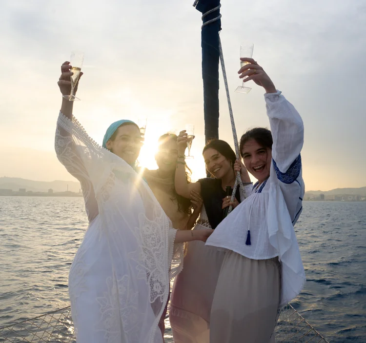 Grupo de amigas brindando con cava al atardecer en un barco frente al skyline de Barcelona