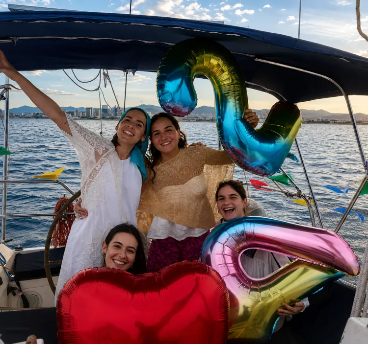 Grup d’amigues celebrant un aniversari en un veler privat a Barcelona amb globus de colors al capvespre